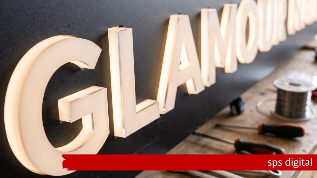 Illuminated 3D lettering mounted on a dark fascia, glowing with bright internal LED light, shown on a workshop bench with tools and wiring in the foreground, capturing precise craftsmanship, clean fabrication detail and a premium SPS Digital illuminated‑signage production environment.